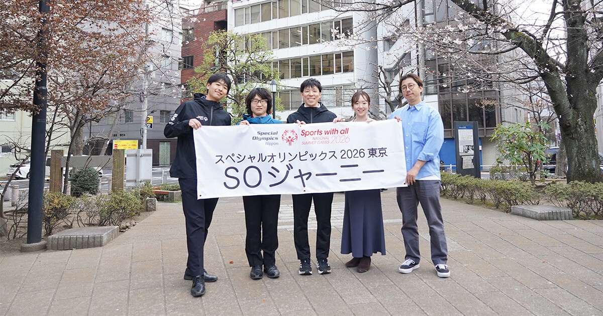 集合写真（前編）：SON様オフィスをバックに桜の咲き始めた公園で、対談メンバー（左から）猪熊氏、仲江氏、三上氏、佐藤、森が笑顔で「スペシャルオリンピックス2026東京」、「SOジャーニー」と書かれた横断幕を持っている様子