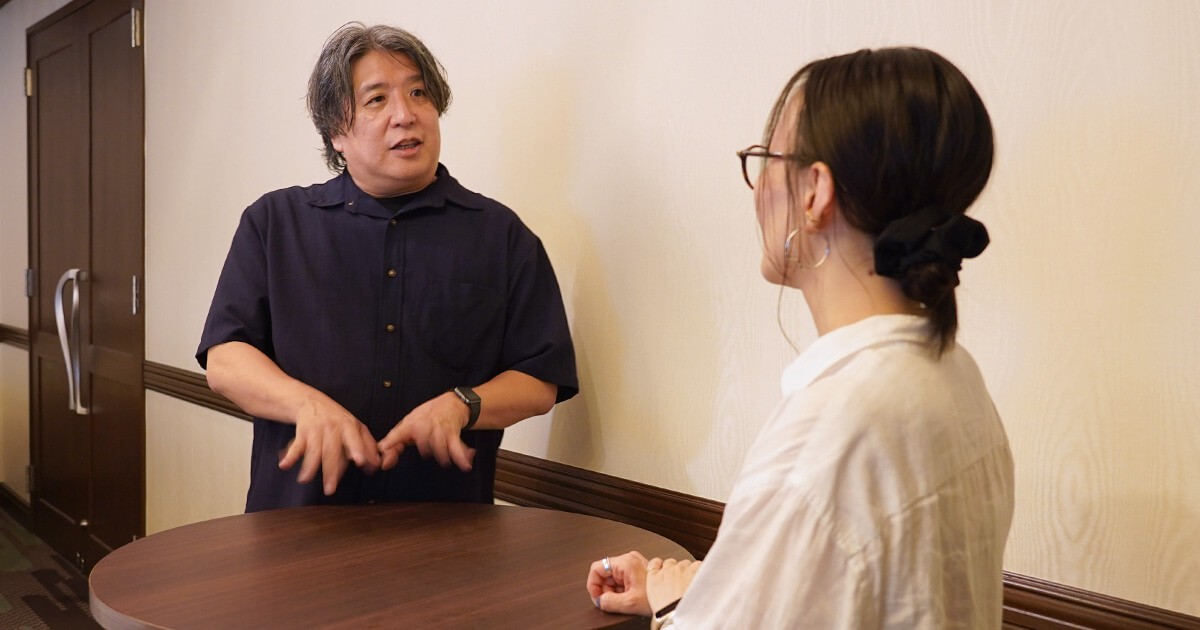 会話風景（小山が話し、新山が聞く様子）